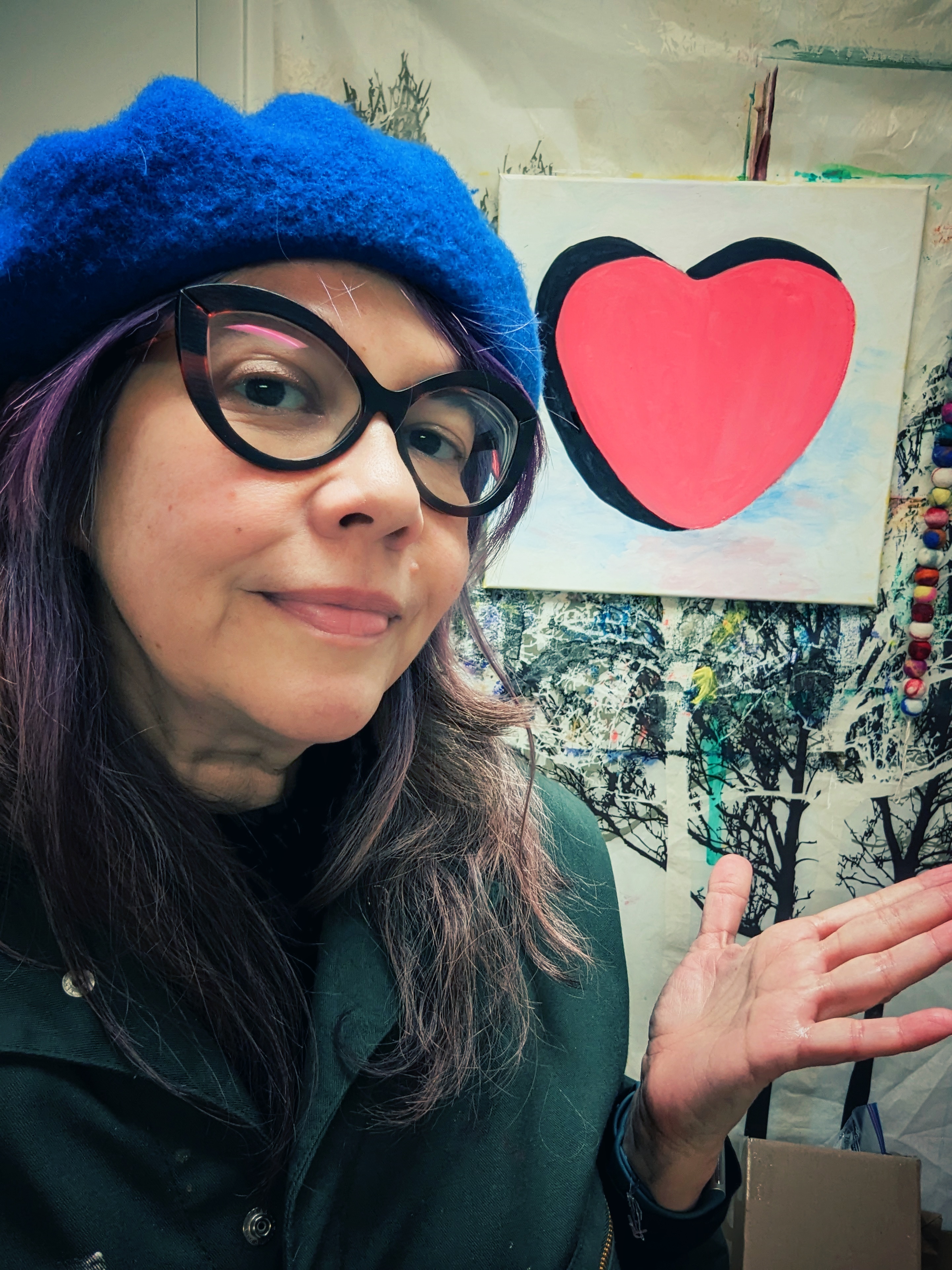  A white woman with purple hair, standing in front of a painting of a heart