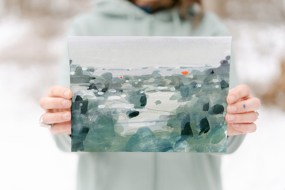 A picture of the artist outside, holding up a small landscape painting.