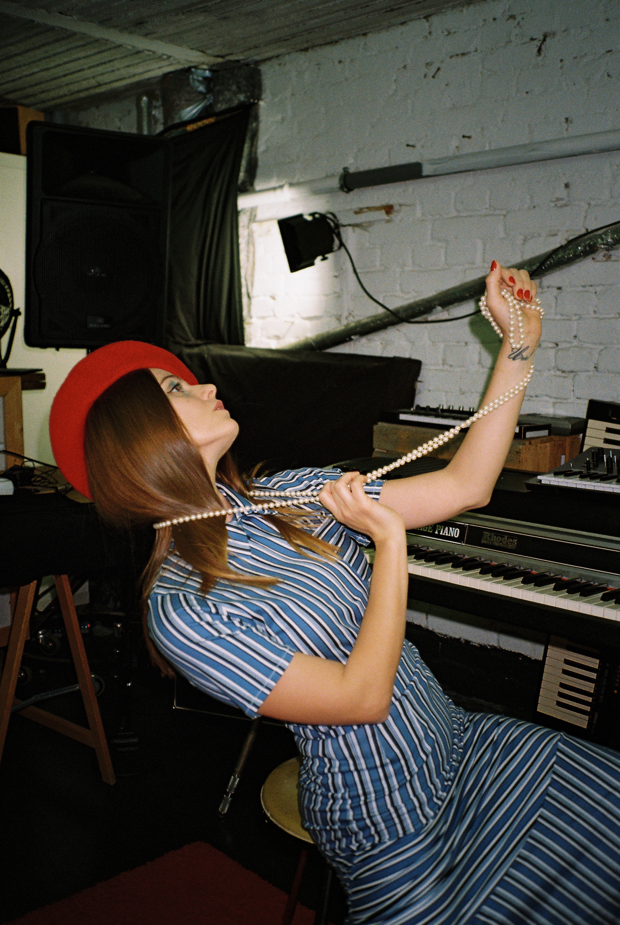 Ati wearing a striped set and red beret, holding out a string of pearls around her neck