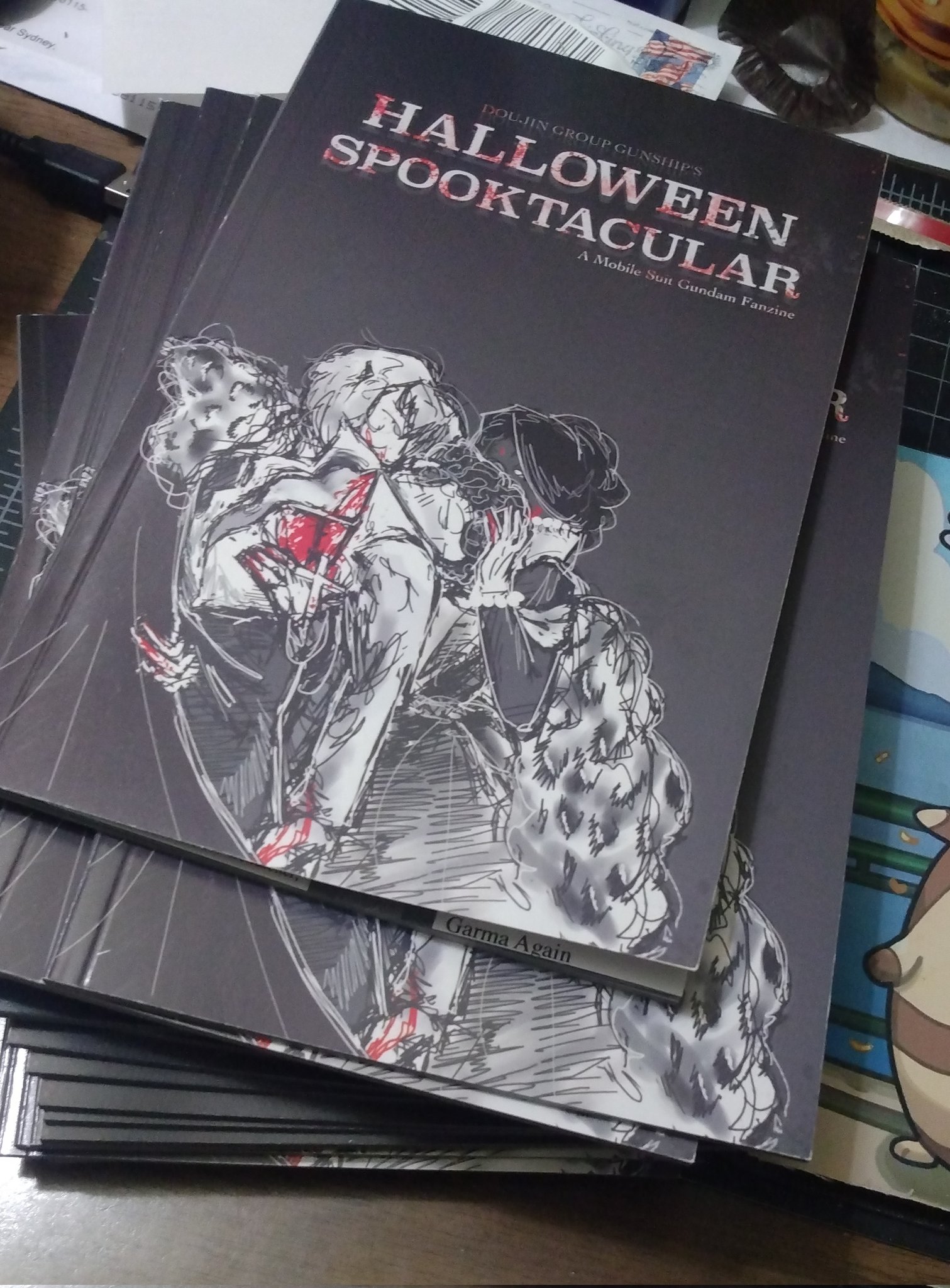 A pile of zines showing off the cover of DGG's Halloween Spooktacular. It's Amuro Ray from Gundam 0079 sandwiched between Char Aznable and Lalah Sune, also from Gundam 0079, except they're vampires since this is a Spooky Publication 