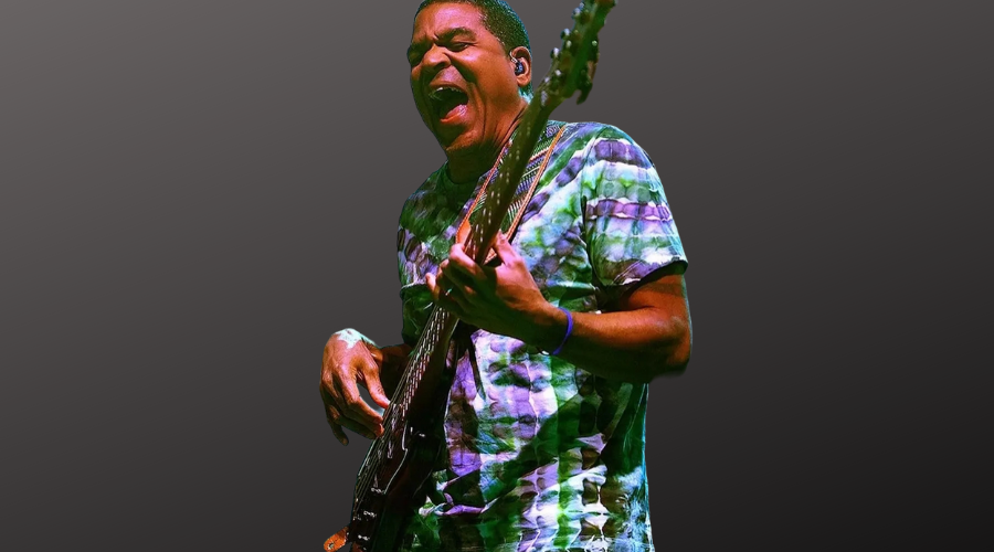 Photo of Oteil Burbridge playing bass guitar and wearing colorful blue and green tie dye tshirt.