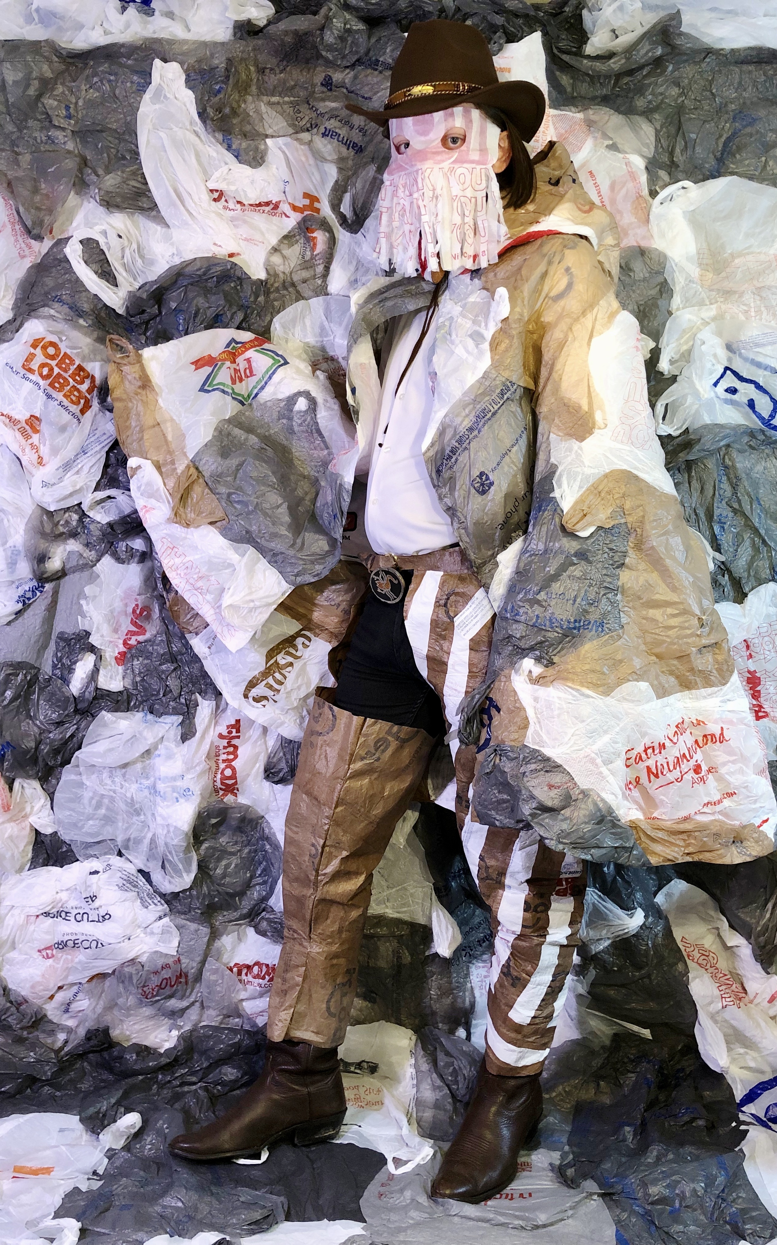 Griffin Nordstrom costumed in a cowboy duster and fringed mask made entirely of reclaimed plastic bags in front of a plastic bag background