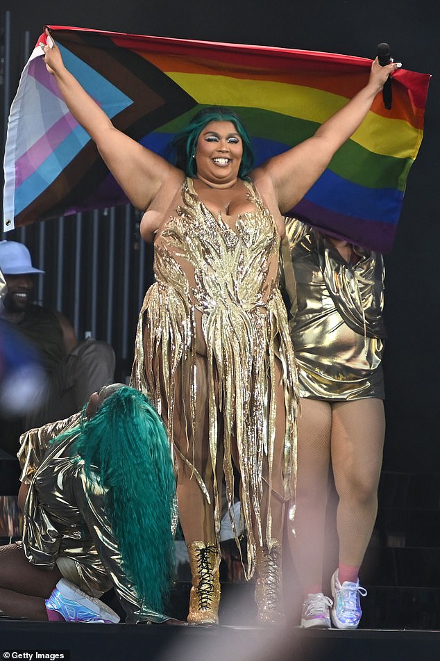 Lizzo in a gold hassled dress holds a rainbow flag