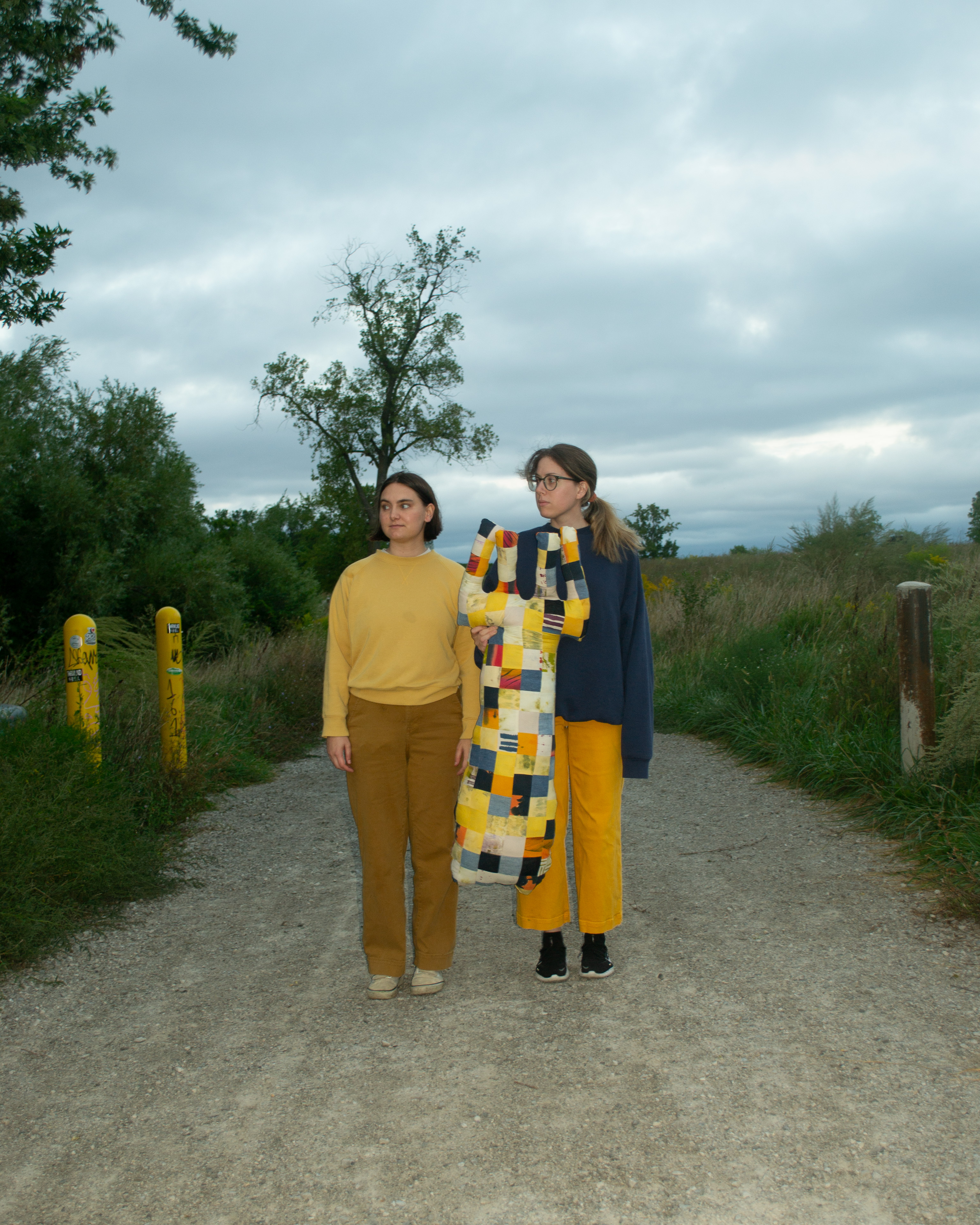 Danielle and Amira stand in a path on Belle Isle holding a large stuffed fork.