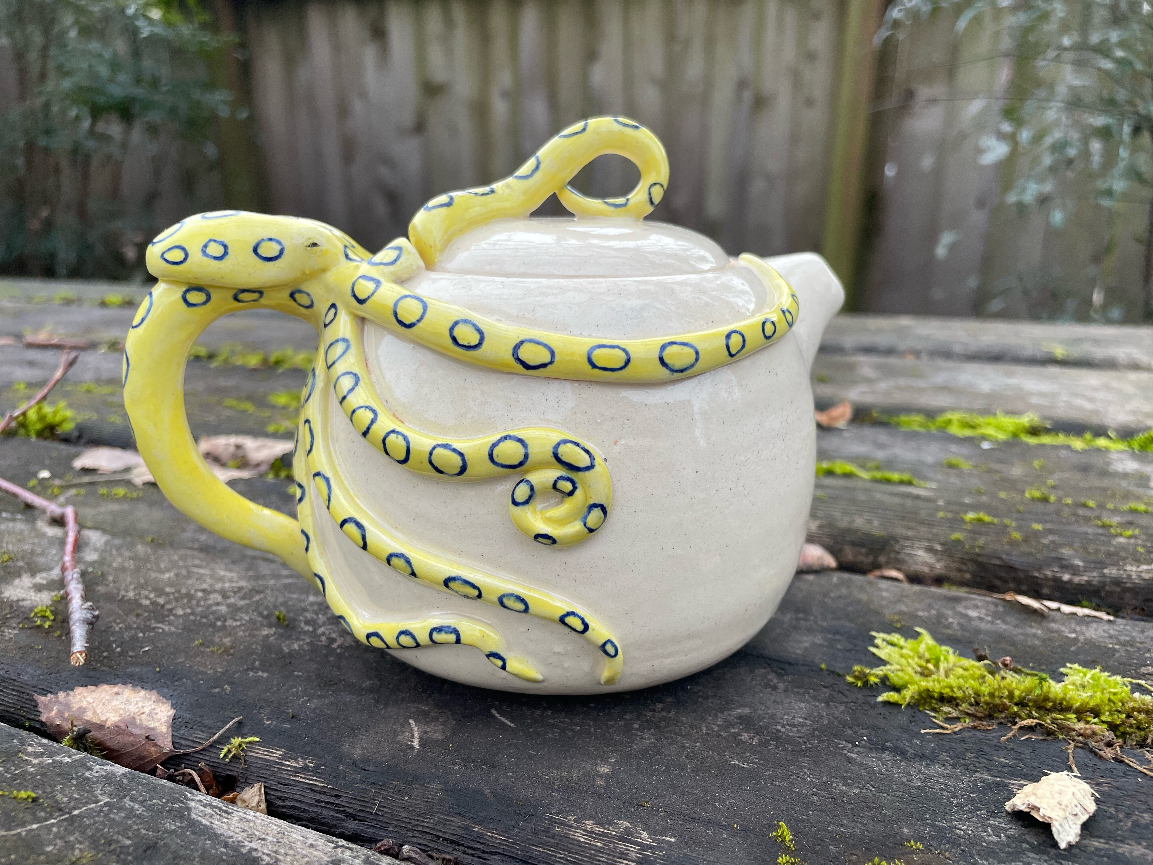 Ceramic teapot with a blue ringed octopus carved around it, one of the tentacles is the handle