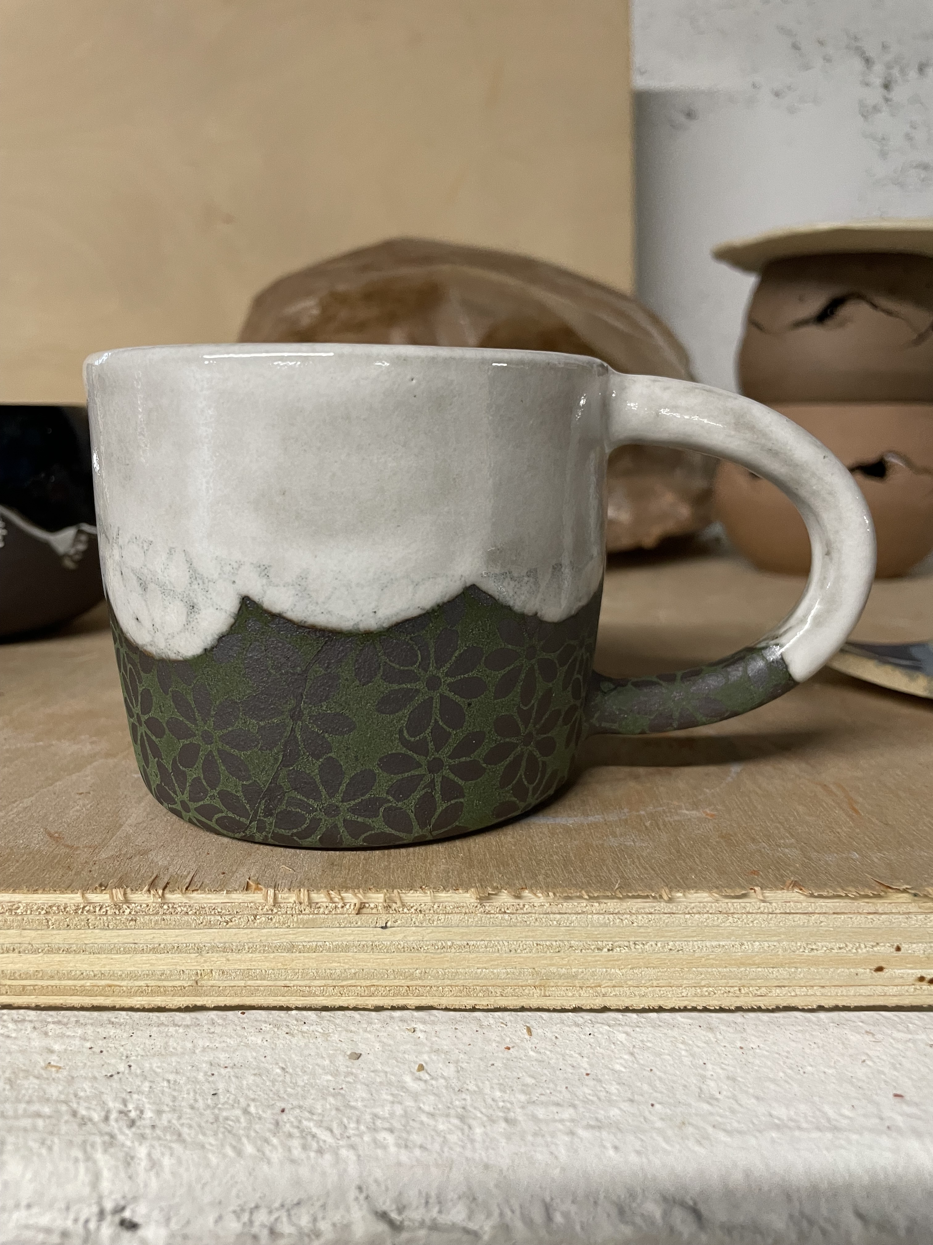 Mug with a white scalloped glaze coming down from the top, at the bottom is a dark clay covered with flower underglaze designs.