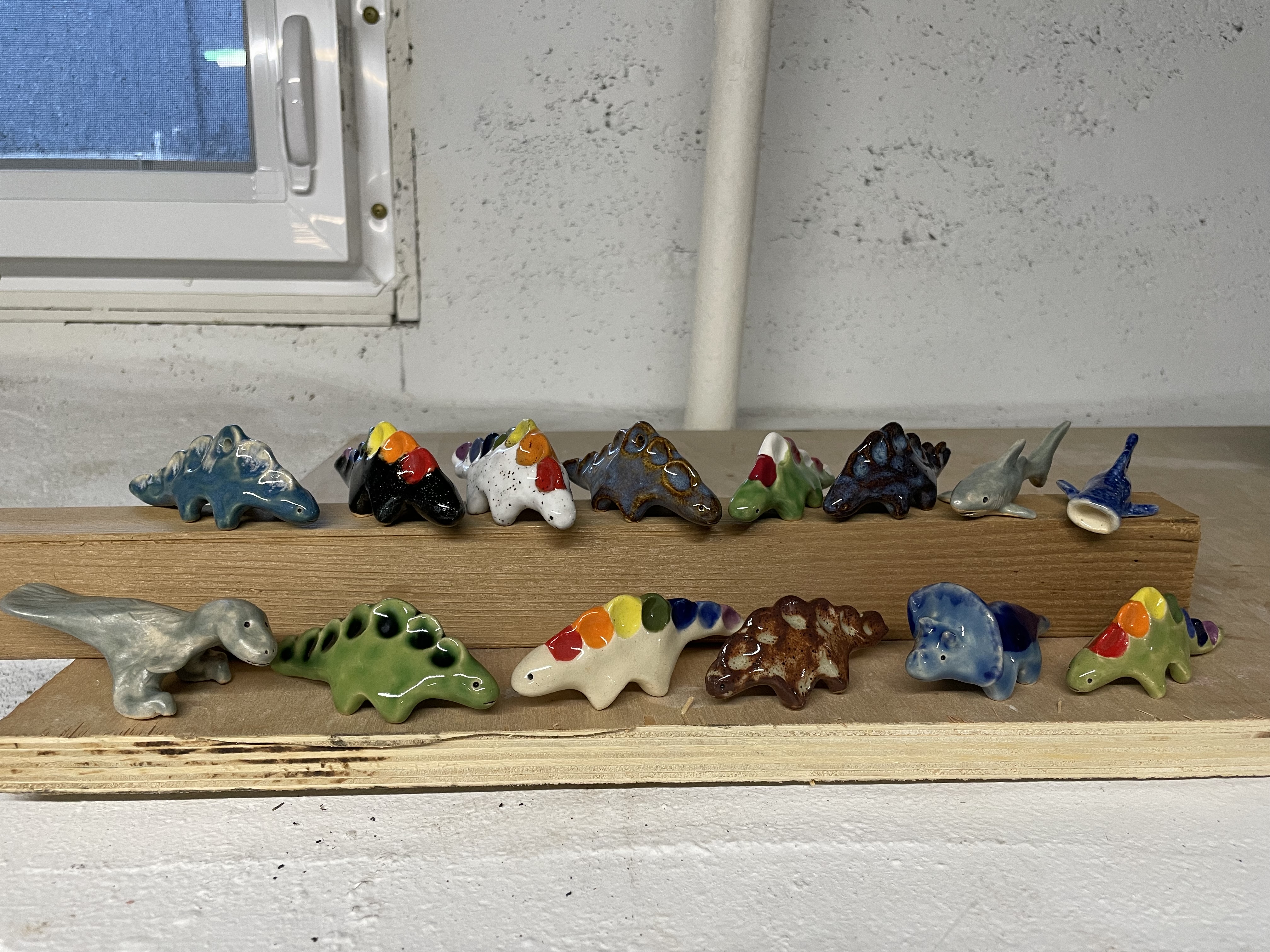 Assortment of small dinosaurs and sea creatures lined up in two rows. They are different colors, some of the stegosauruses have rainbow painted spines.