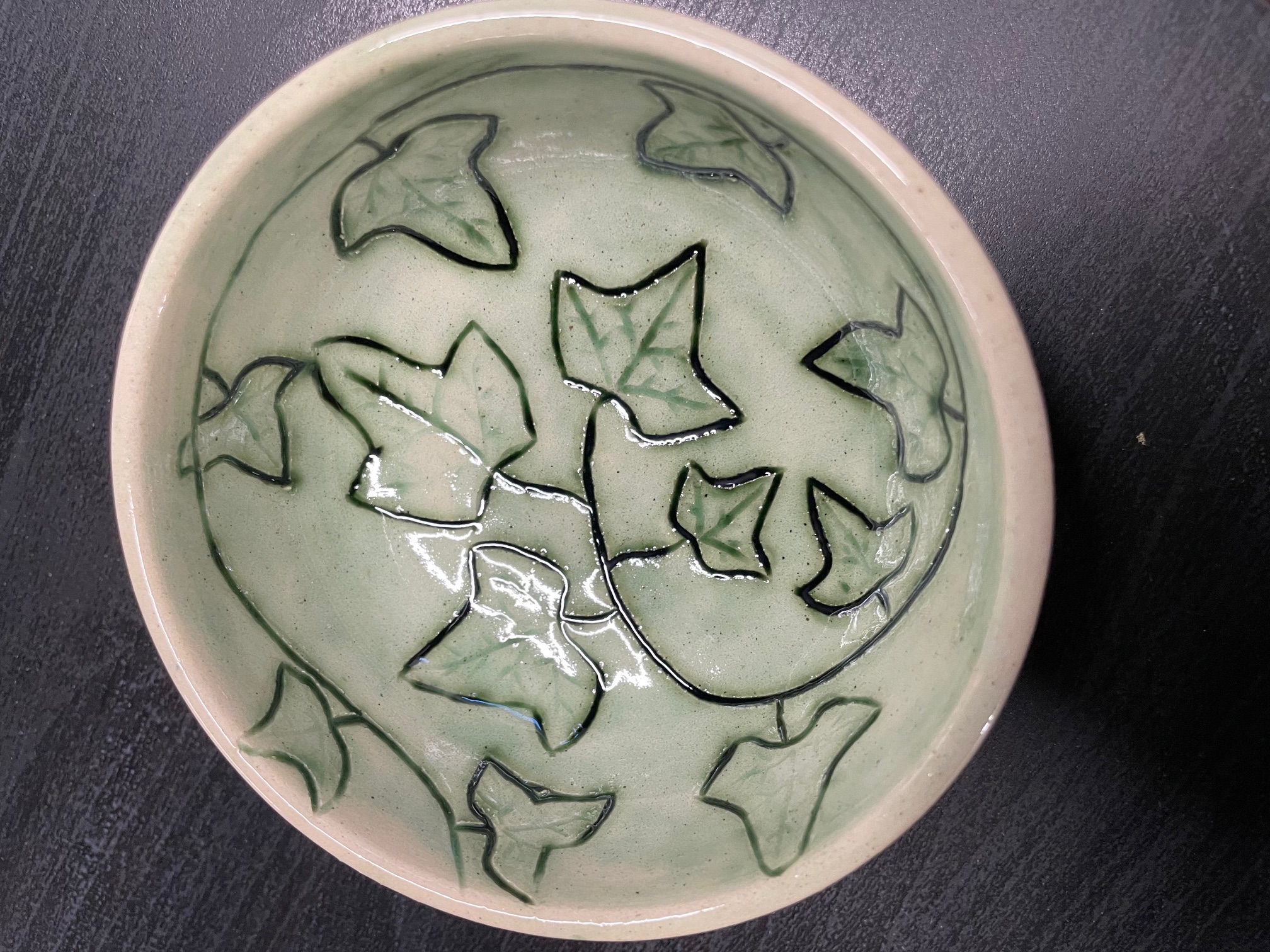 Pale green and white bowl with carved, dark green ivy leaves in a spiral inside the bowl.