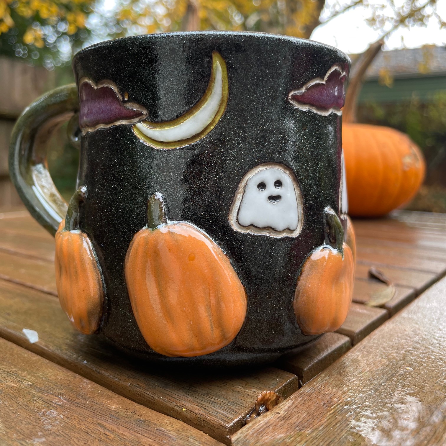 Mug with carved pumpkins, clouds, crescent moon, and a ghost on a glittery black background.