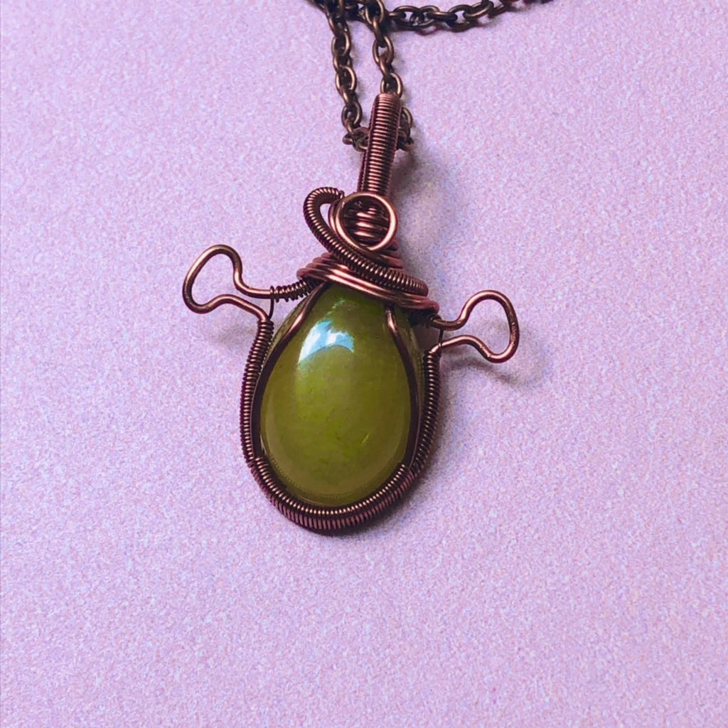 Copper wire wrapped green stone pendant with Shrek ears on pink background 