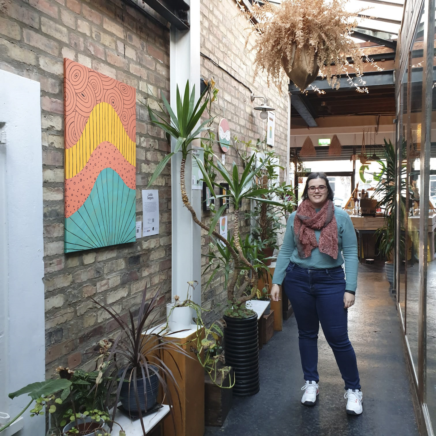 Lucia Segura Art posing with her artworks in Nomadis Café, London, 2021.