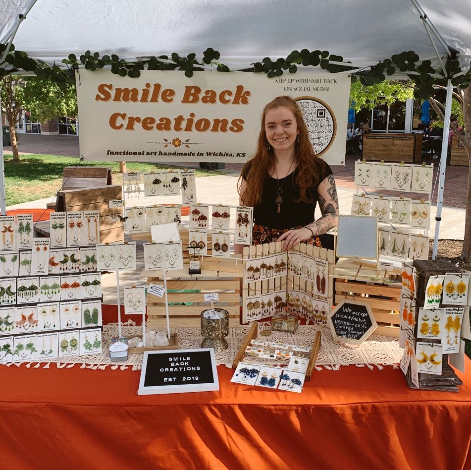 The artist (madison) standing in front of her market display containing multiple displays of different colored earrings