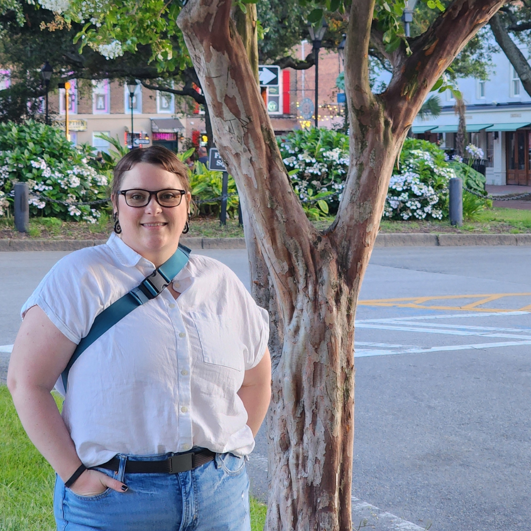 Sarah Householder owner of The Witty Ladybug stands in front of a Tree and a square in Savannah, GA