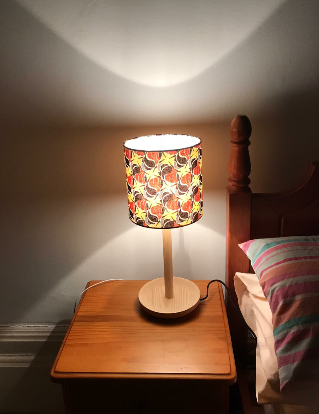 Small bedside table patterned with mixed brown & yellow seeds on an African print fabric. The light is switched on too