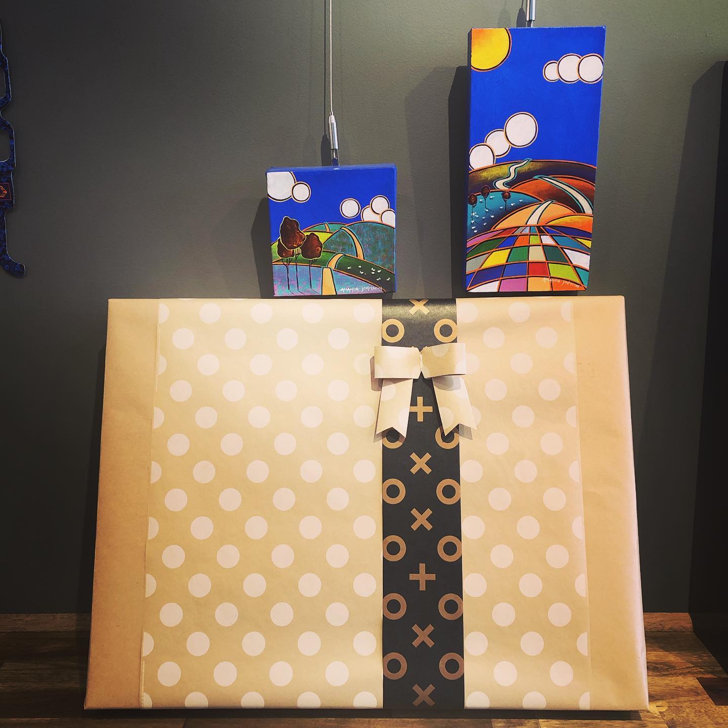 A gift wrapped painting sits below 2 of Amanda's original works in the gallery space at WNA