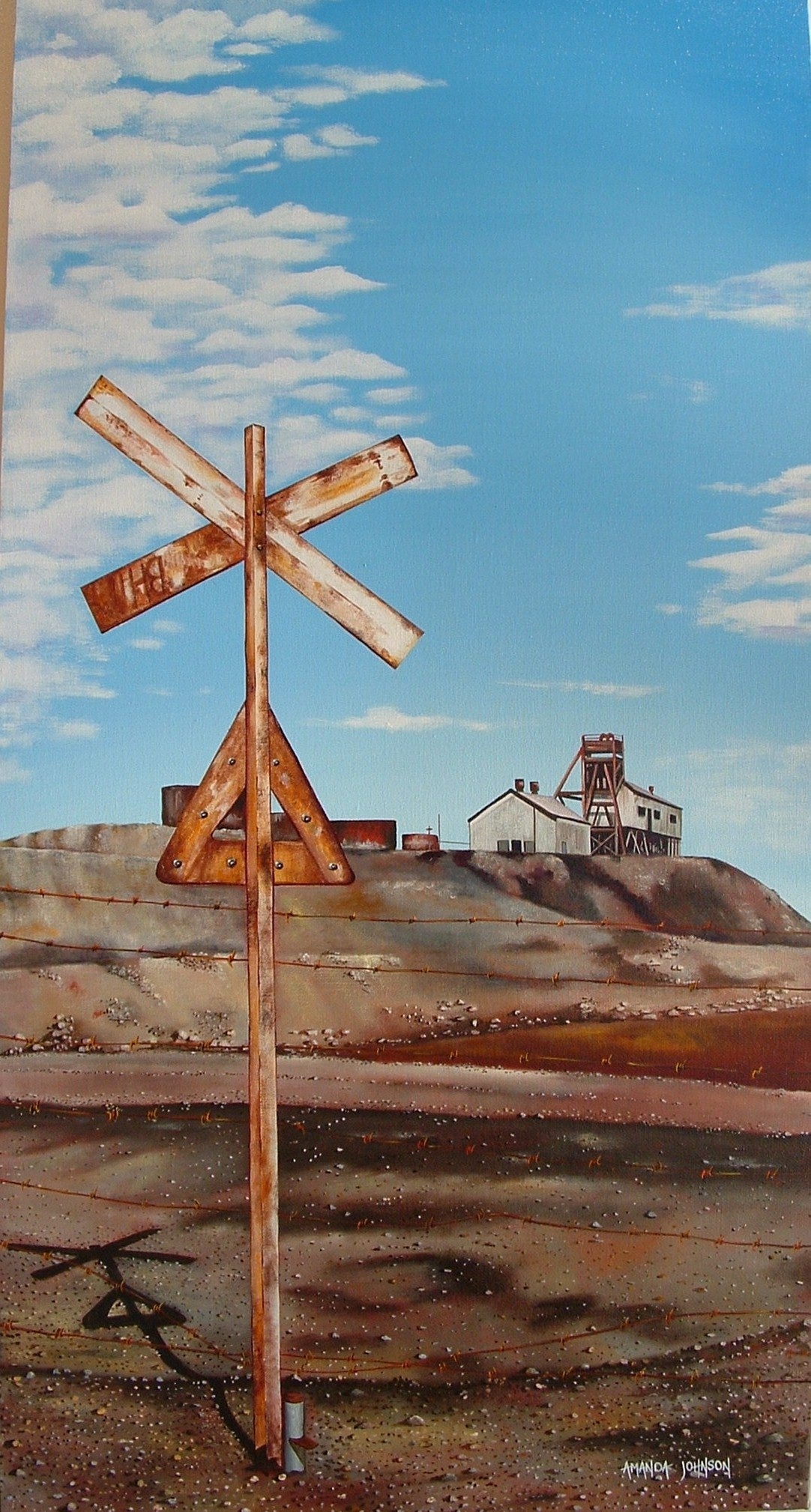 The back of a rail crossing sign in the foreground and a mine headframe and buildings in the background with red and brown tones of earth in between