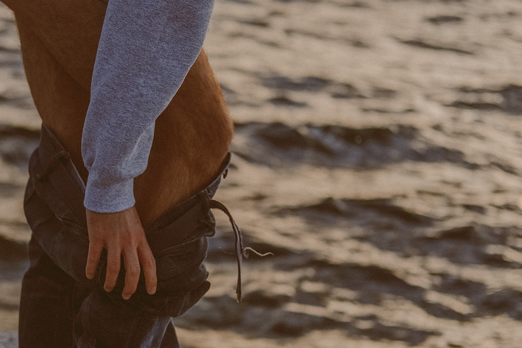 Picture of a man taking off his jeans in front of the water cropped from below his butt to above the ankles.
