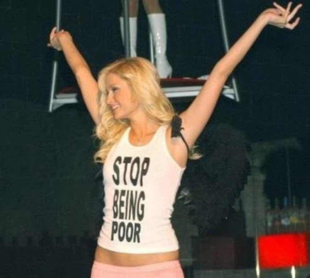 Paris `Hilton raising her arms wearing a white tank top which says 'Stop Being Poor'