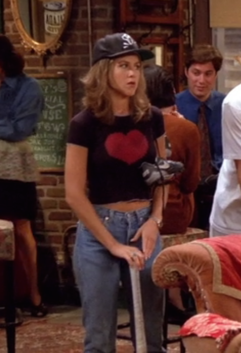Rachel Green standing in a baseball cap, cropped black tee with a red heart and blue mom jeans holding a baseball bat.