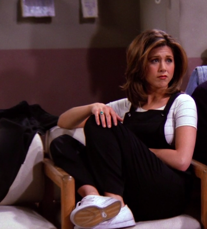 Rachel Green Sat on a chair in a white stripes top with black dungarees and white plimsolls