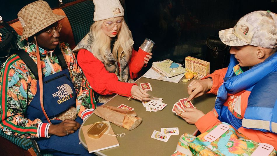 Two men and a woman playing cards wearing brightly coloured ski style clothing from The North Face X Gucci