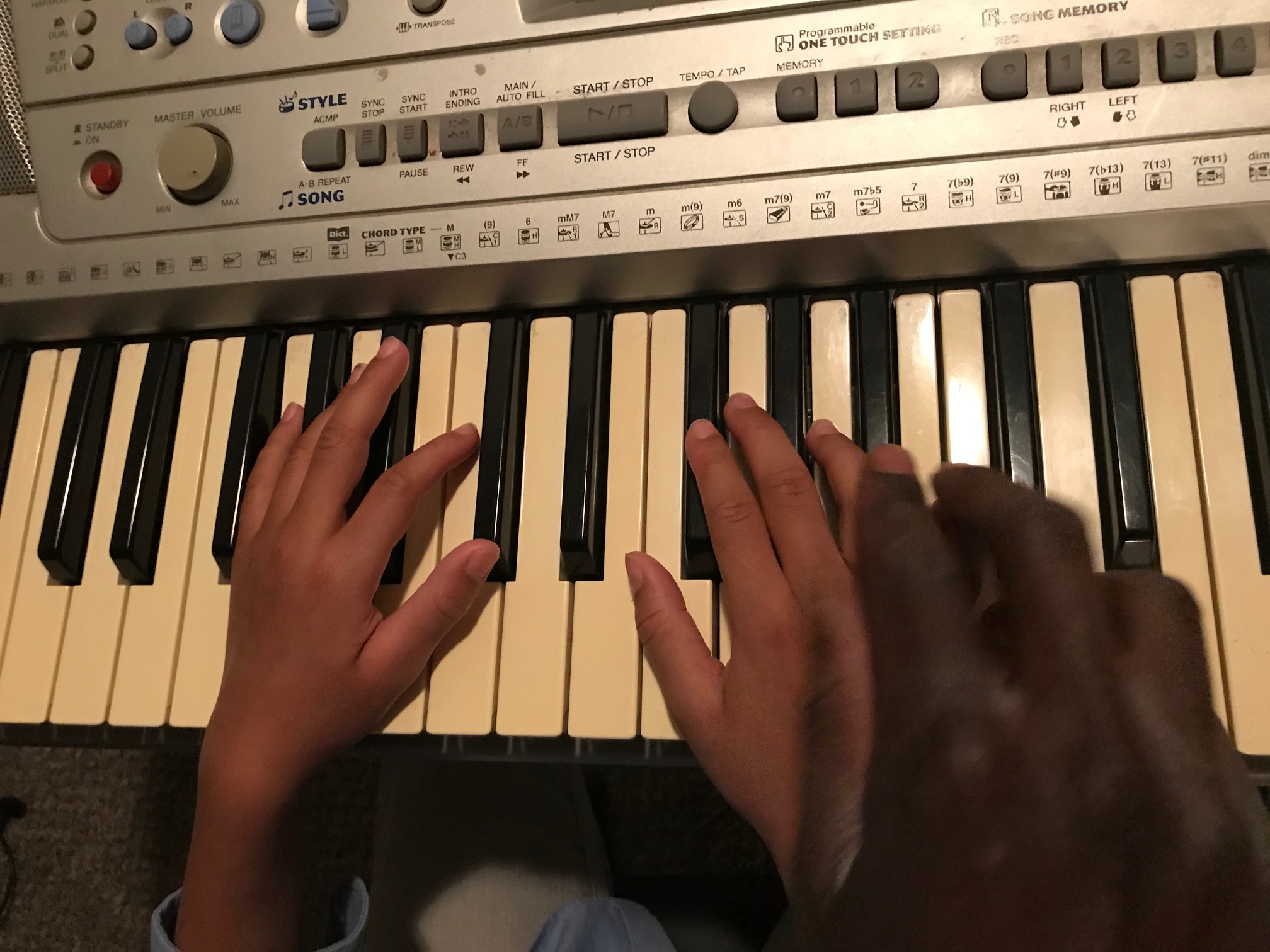a piano teacher hand over a child hand while playing piano keys.