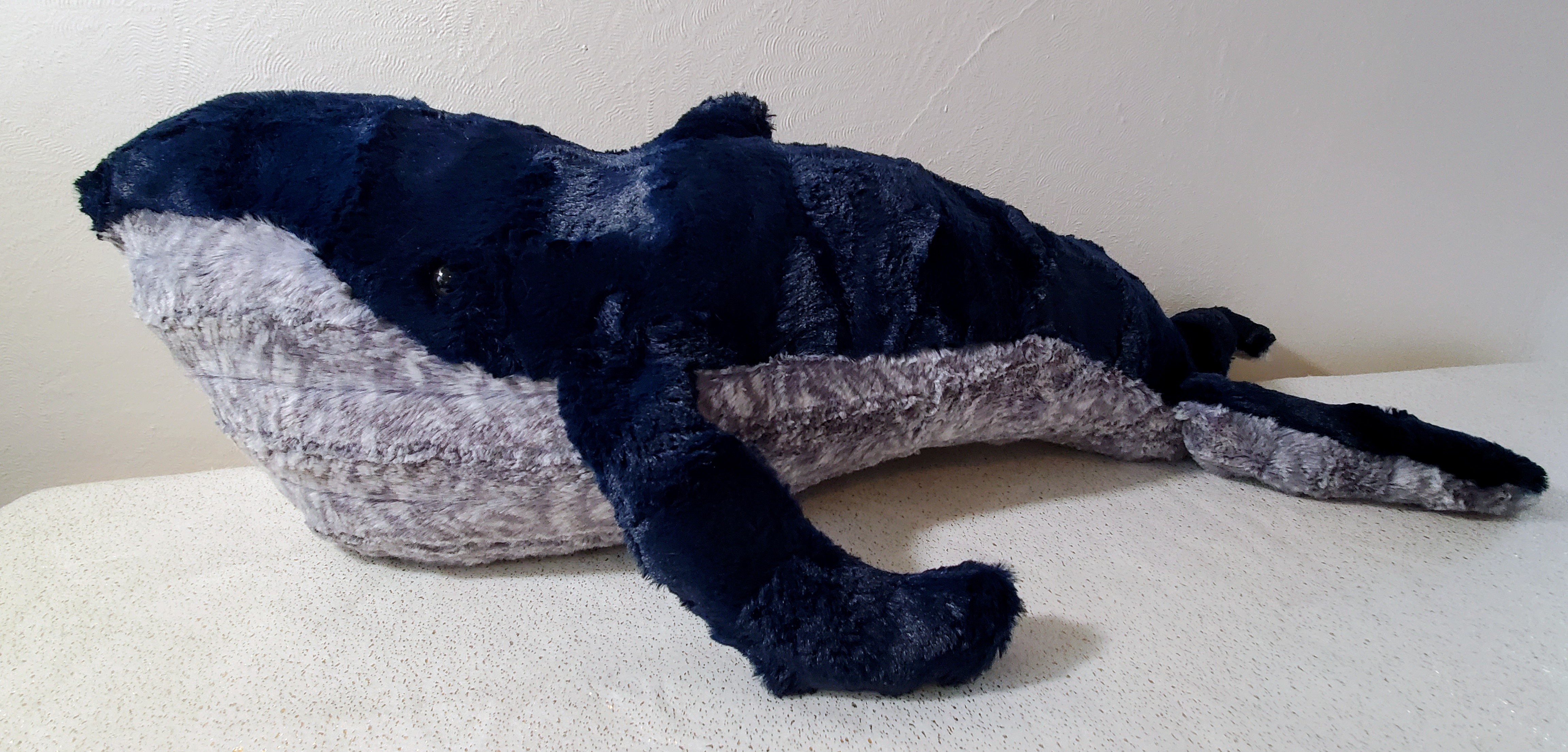 Image of a fluffy whale plush–navy on top, striped grey on the bottom.