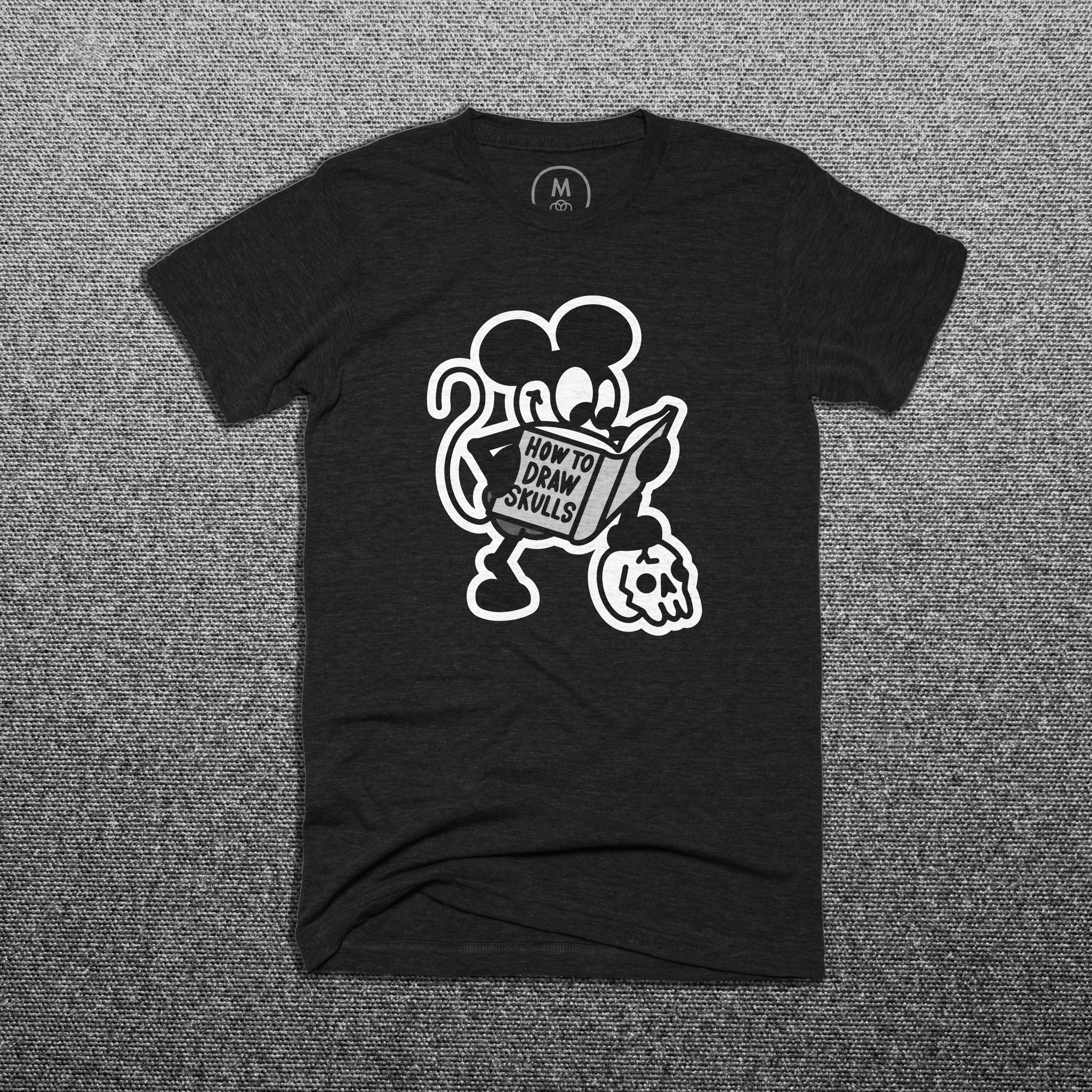 a black t-shirt with mickey mouse standing with one foot on a skull reading a book called "how to draw skulls"