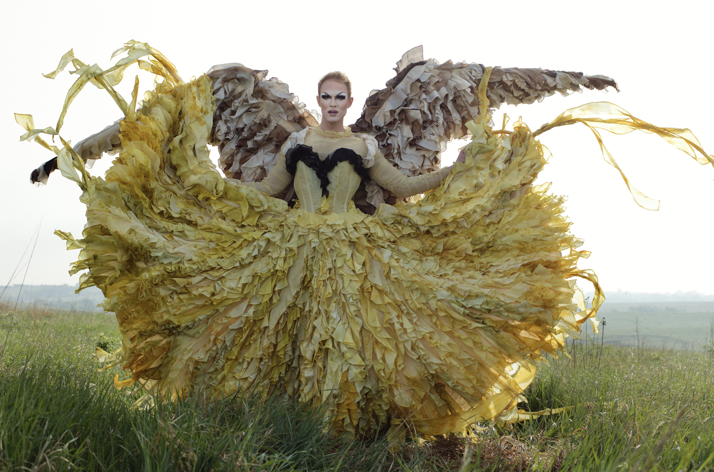 Pattie Gonia wears a dress with naturally dyed yellow ruffles and large wings dyed with walnut.