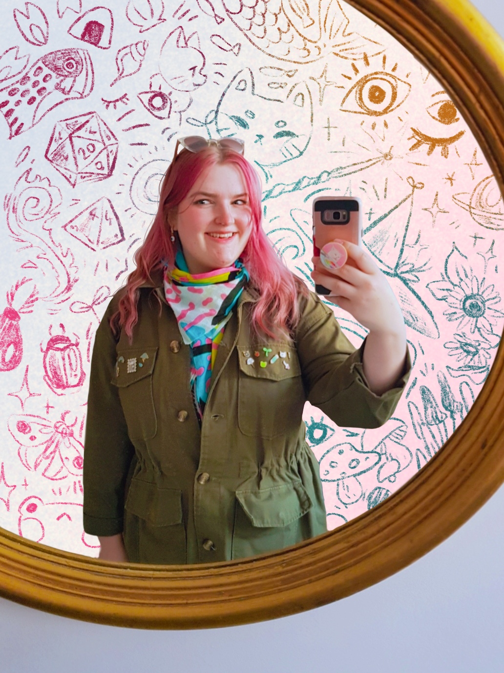A mirror selfie of the artist. She is smiling, wearing a olive green jacket with pins on the chest pockets. She has pink hair. In the background are sketchy drawings of items such as, cats, dice, flowers, mushrooms and more.
