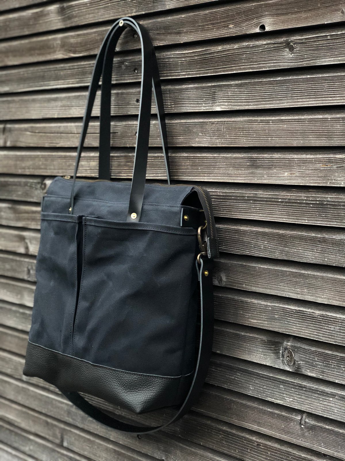 Black waxed canvas tote bag with leather bottom handles and cross