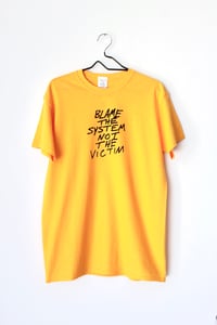 Image of blame the system not the victim tee in yellow