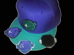 Image of Purple and turquoise cap with 2 badges (turquoise/purple and turquoise badge)