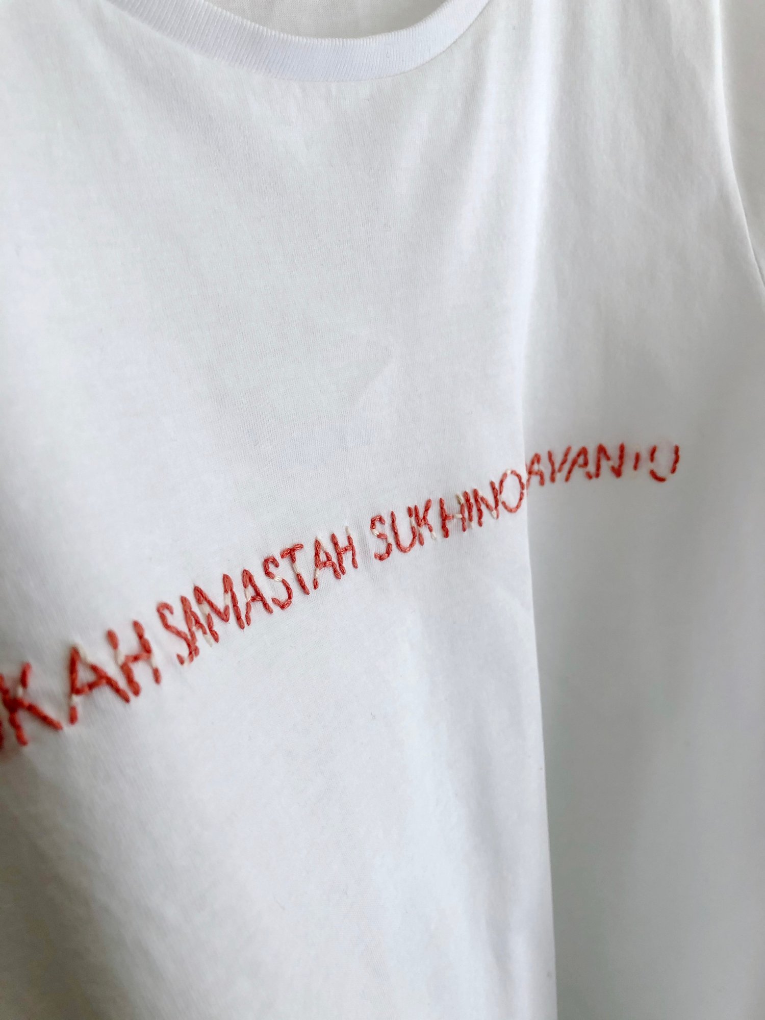 Image of LOKAH SAMASTAH SUKHINO BHAVANTU – red/beige – white t-shirt w/ rolled-up sleeves – 