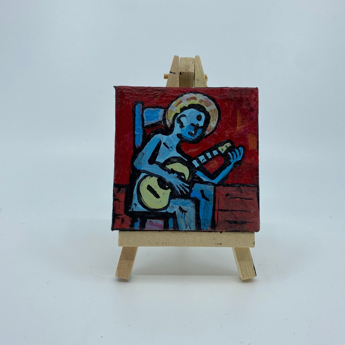 Image of haloed blue being tuning a guitar while sitting on blue chair in a red room with a wooden floor