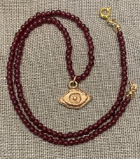 Image 2 of Bronze Averting Eye pendant on a string of garnets.