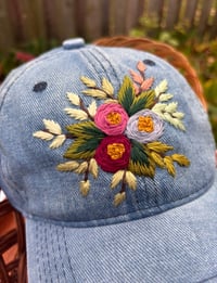 Image 2 of Dark maroon, pink, and light purple hand embroidered flowers on an adjustable medium blue colour hat