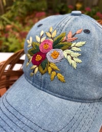 Image 3 of Dark maroon, pink, and light purple hand embroidered flowers on an adjustable medium blue colour hat