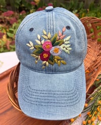 Image 1 of Dark maroon, pink, and light purple hand embroidered flowers on an adjustable medium blue colour hat