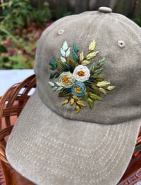 Image 3 of Blue, white, and light green hand embroidered flowers on an adjustable khaki fabric hat