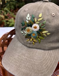Image 4 of Blue, white, and light green hand embroidered flowers on an adjustable khaki fabric hat