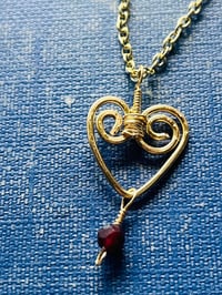 Image 1 of wire wrapped heart with tiny garnet in gold