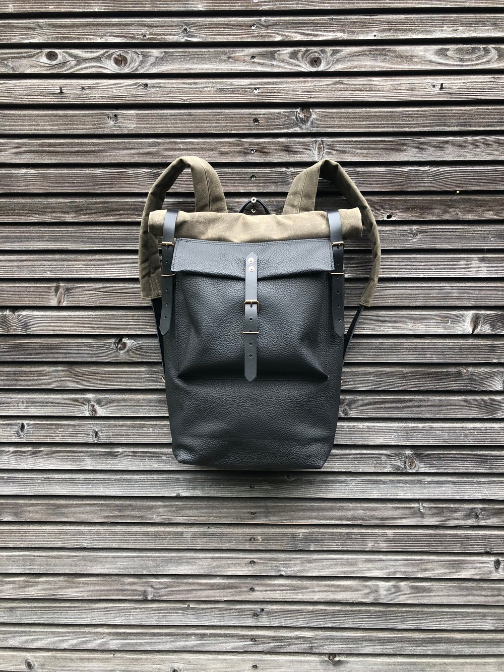 Image of Black leather backpack with waxed canvas roll to close top and leather front pocket