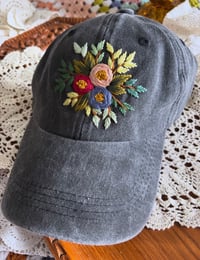 Dark red, blue, and light pink hand embroidered flowers on an adjustable dark grey fabric hat 