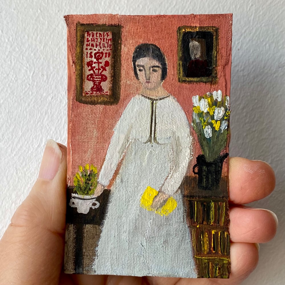 Image of woman with yellow book and sampler on the wall