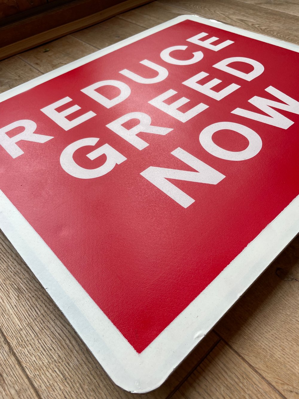 Image of REDUCE GREED NOW METAL ROAD SIGN