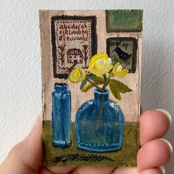 Image of still life with bottles, roses and stitched samplers